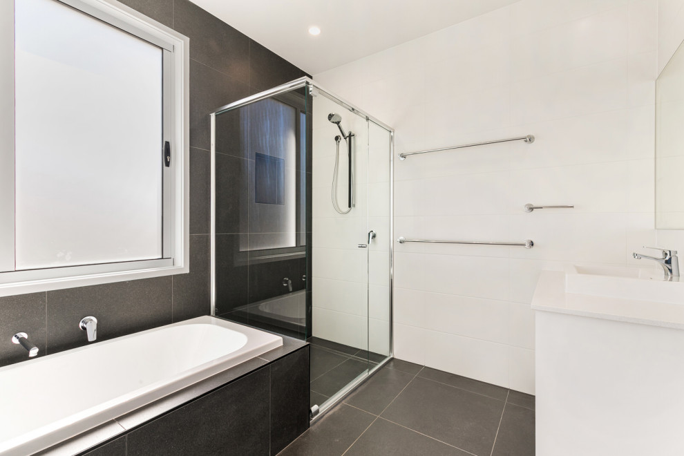 Idéer för att renovera ett mellanstort funkis vit vitt badrum med dusch, med släta luckor, vita skåp, ett hörnbadkar, en hörndusch, vit kakel, keramikplattor, vita väggar, klinkergolv i keramik, ett nedsänkt handfat, bänkskiva i kvarts, svart golv och dusch med gångjärnsdörr