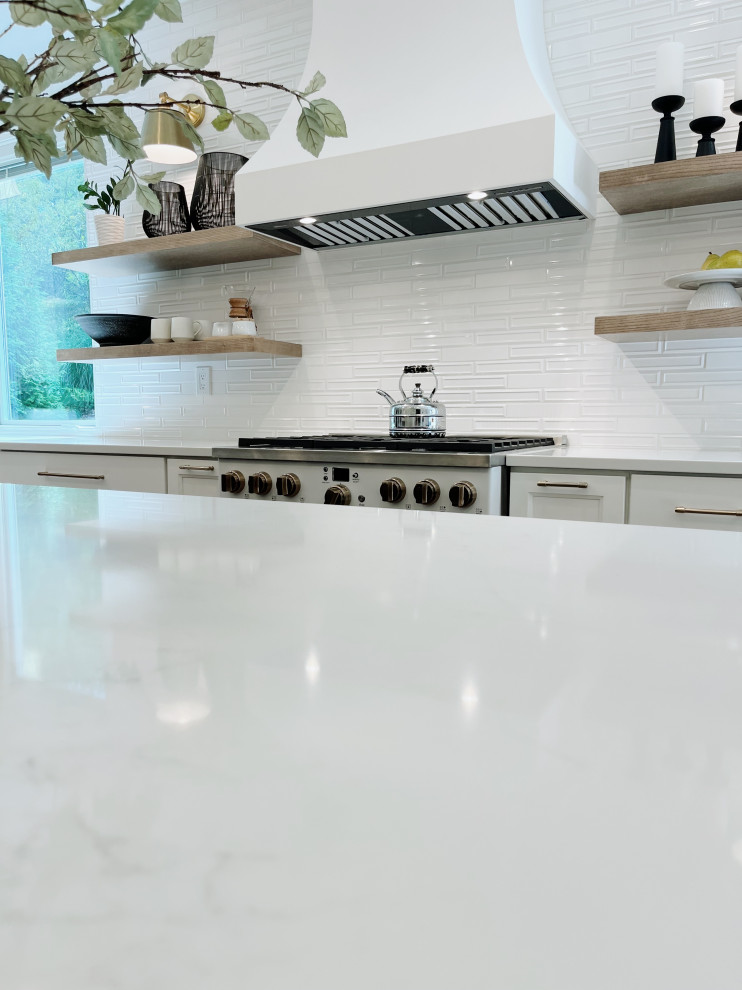 Large transitional l-shaped light wood floor and beige floor eat-in kitchen photo with a farmhouse sink, shaker cabinets, white cabinets, quartz countertops, white backsplash, ceramic backsplash, white appliances, an island and white countertops