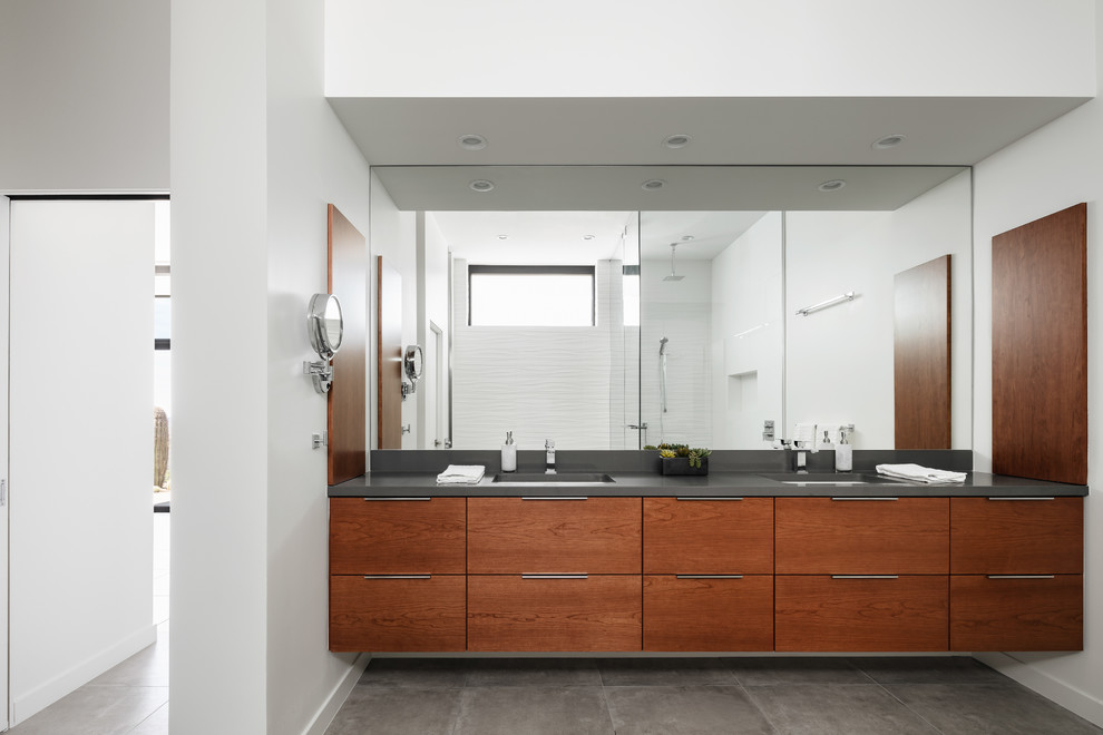 Inspiration for a contemporary master bathroom in Phoenix with flat-panel cabinets, medium wood cabinets, a freestanding tub, a corner shower, a wall-mount toilet, white tile, ceramic tile, white walls, porcelain floors, an undermount sink, engineered quartz benchtops, grey floor, a hinged shower door and grey benchtops.