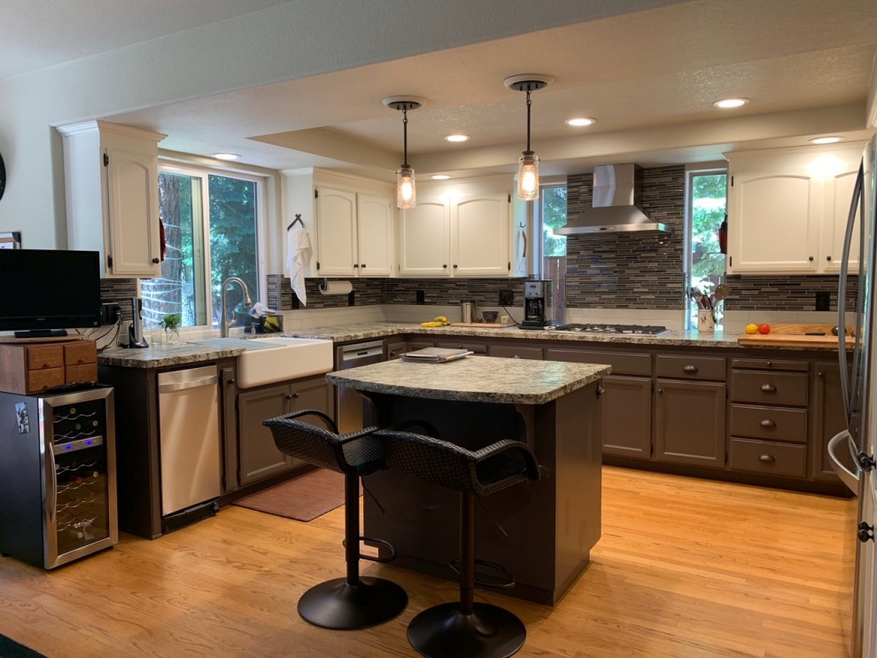 Eat-in kitchen - mid-sized transitional u-shaped light wood floor and yellow floor eat-in kitchen idea with a farmhouse sink, recessed-panel cabinets, brown cabinets, granite countertops, multicolored backsplash, glass sheet backsplash, stainless steel appliances, an island and multicolored countertops