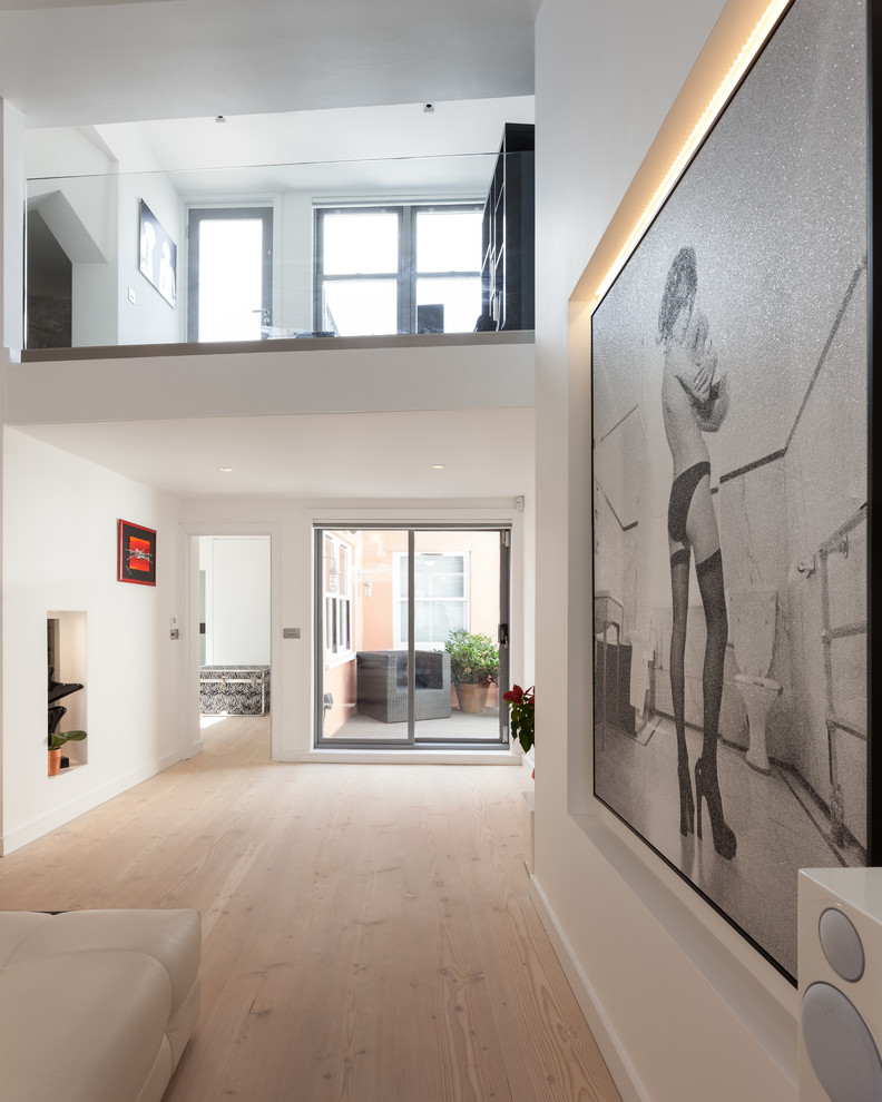 This is an example of a mid-sized contemporary formal open concept living room in London with white walls, light hardwood floors, a wall-mounted tv and white floor.