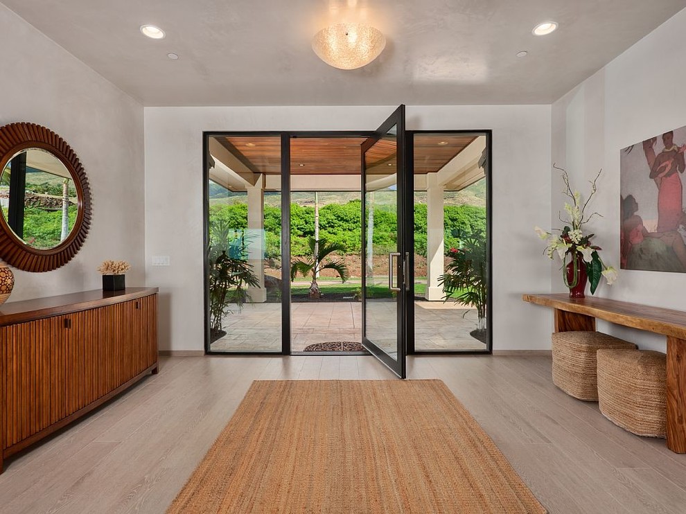 Mid-sized tropical front door in Hawaii with a pivot front door, a glass front door, white walls, light hardwood floors and beige floor.