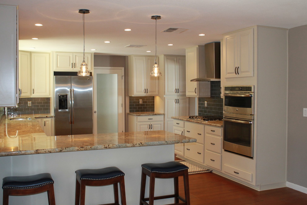 Eat-in kitchen - mid-sized transitional u-shaped dark wood floor and brown floor eat-in kitchen idea in Phoenix with an undermount sink, raised-panel cabinets, white cabinets, granite countertops, green backsplash, glass tile backsplash, stainless steel appliances and a peninsula