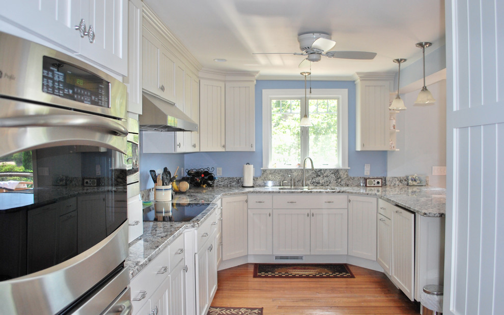 Large beach style u-shaped eat-in kitchen in Portland Maine with an undermount sink, beaded inset cabinets, white cabinets, granite benchtops, stainless steel appliances, dark hardwood floors and with island.