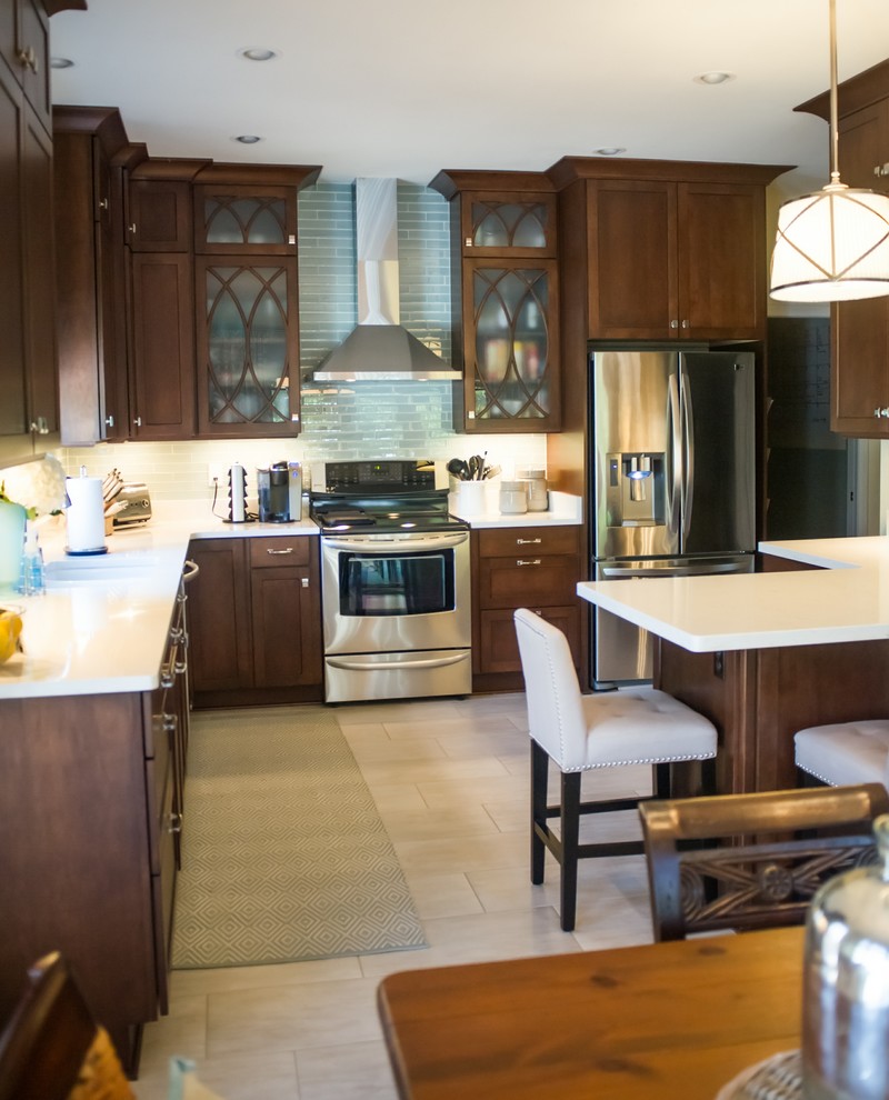 Mid-sized transitional u-shaped eat-in kitchen photo with an undermount sink, dark wood cabinets, blue backsplash, glass tile backsplash, stainless steel appliances and a peninsula