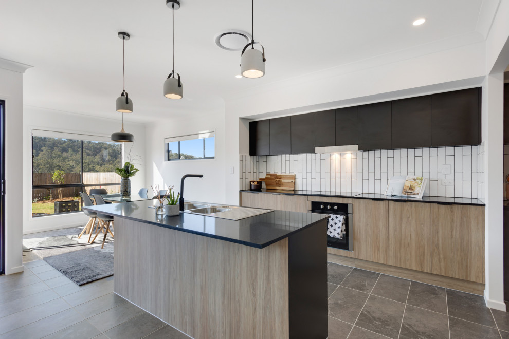 This is an example of a mid-sized contemporary galley open plan kitchen in Brisbane with a double-bowl sink, black cabinets, quartz benchtops, white splashback, ceramic splashback, stainless steel appliances, ceramic floors, with island, grey floor and grey benchtop.