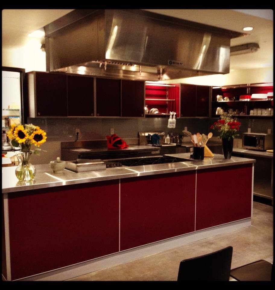 バンクーバーにあるインダストリアルスタイルのおしゃれなアイランドキッチン (フラットパネル扉のキャビネット、赤いキャビネット、ステンレスカウンター、シルバーの調理設備) の写真