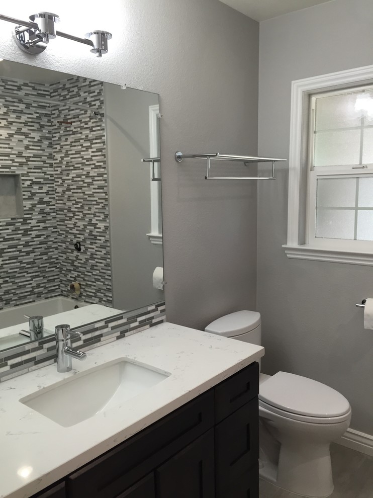 Mid-sized transitional bathroom in San Francisco with an undermount sink, shaker cabinets, dark wood cabinets, engineered quartz benchtops, an alcove tub, a shower/bathtub combo, a two-piece toilet, gray tile, porcelain tile, grey walls and porcelain floors.