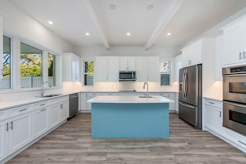 This is an example of a traditional kitchen in Miami with white cabinets, white splashback, stainless steel appliances, with island, white benchtop and exposed beam.
