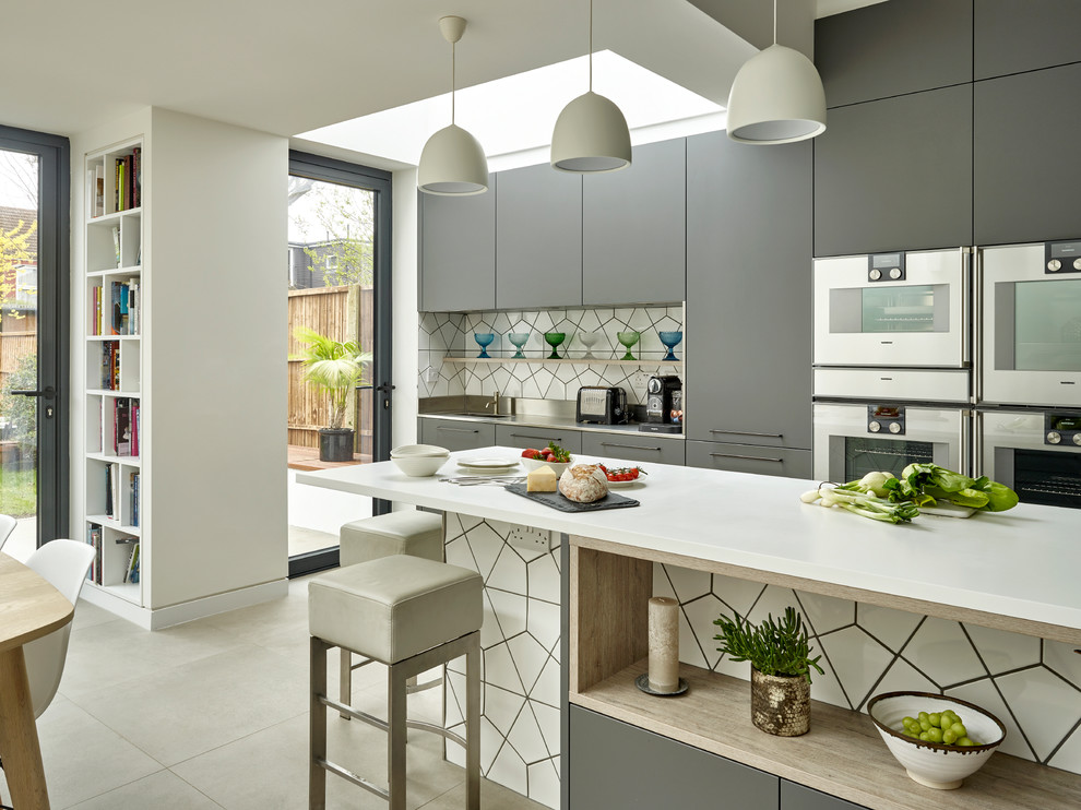 Contemporary single-wall eat-in kitchen in London with flat-panel cabinets, grey cabinets, solid surface benchtops, white splashback, ceramic splashback, stainless steel appliances, ceramic floors, with island and grey floor.