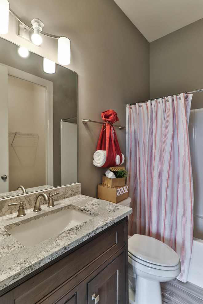 Inspiration for a mid-sized transitional 3/4 bathroom in St Louis with shaker cabinets, dark wood cabinets, an alcove tub, a shower/bathtub combo, a two-piece toilet, white tile, porcelain tile, beige walls, vinyl floors, an undermount sink, granite benchtops, grey floor and a shower curtain.