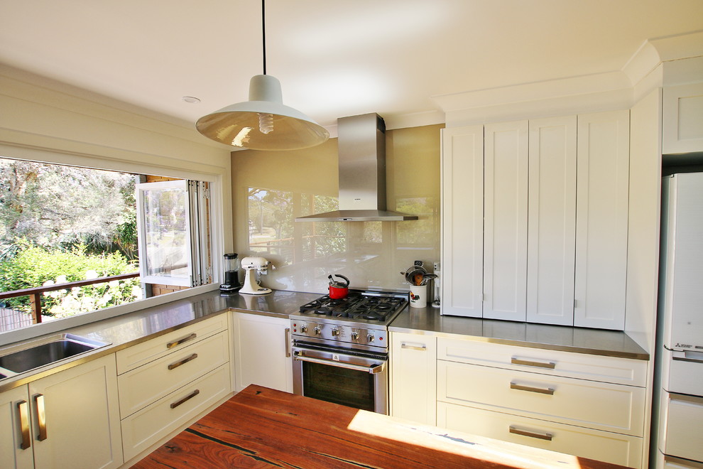 Design ideas for a mid-sized transitional l-shaped kitchen pantry in Sydney with a double-bowl sink, shaker cabinets, white cabinets, stainless steel benchtops, black splashback, glass sheet splashback, stainless steel appliances, light hardwood floors and with island.