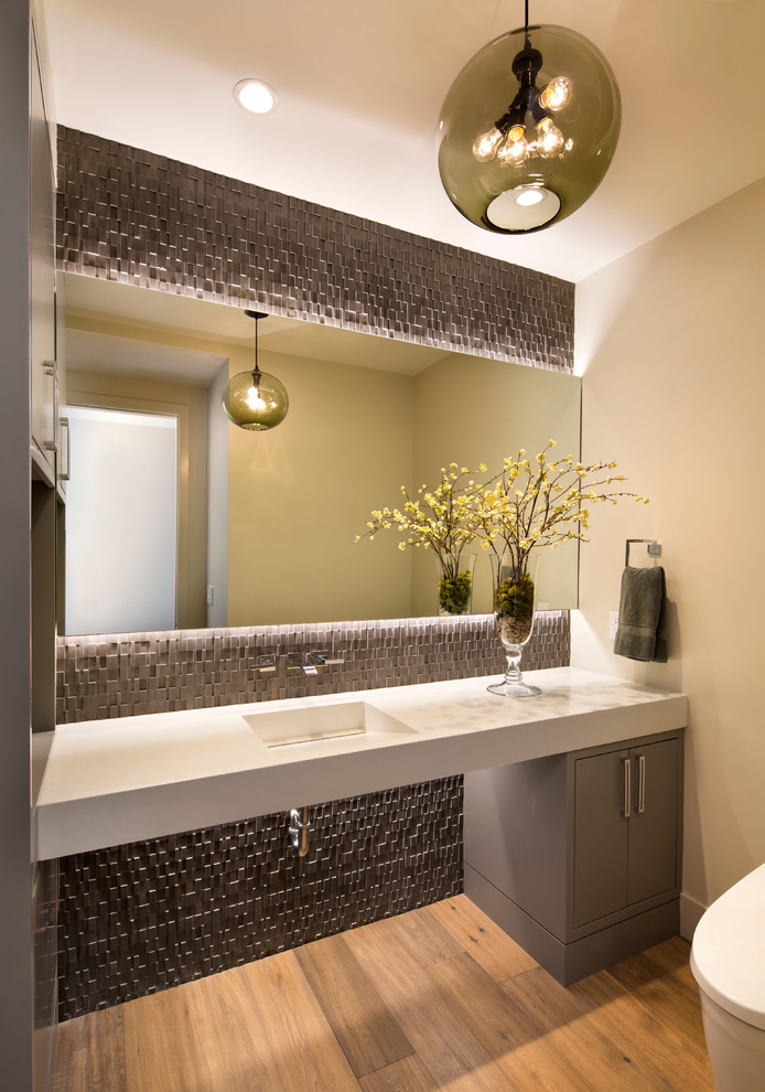 This is an example of a contemporary powder room in San Francisco with flat-panel cabinets, grey cabinets, beige walls, light hardwood floors and an integrated sink.