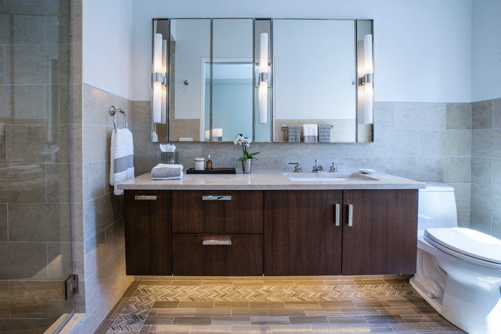 This is an example of a mid-sized contemporary master bathroom in New York with glass-front cabinets, a corner shower, beige tile, marble benchtops, dark wood cabinets, a one-piece toilet, stone tile, white walls, porcelain floors and an undermount sink.
