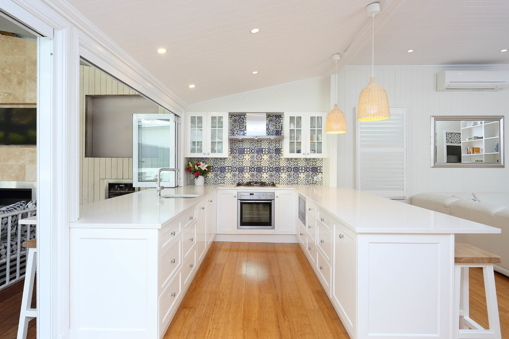 This is an example of a mid-sized traditional galley kitchen in Brisbane with a drop-in sink, shaker cabinets, white cabinets, laminate benchtops, blue splashback, stone tile splashback, stainless steel appliances, bamboo floors and no island.