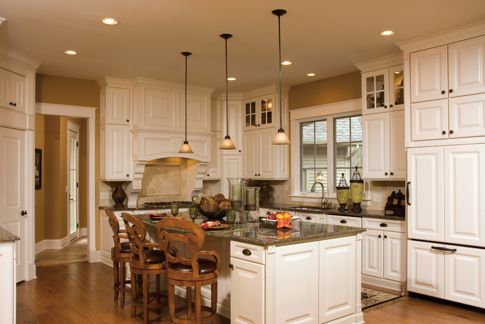 Design ideas for a large traditional l-shaped eat-in kitchen in Indianapolis with raised-panel cabinets, white cabinets, granite benchtops, beige splashback, ceramic splashback, white appliances, medium hardwood floors and with island.