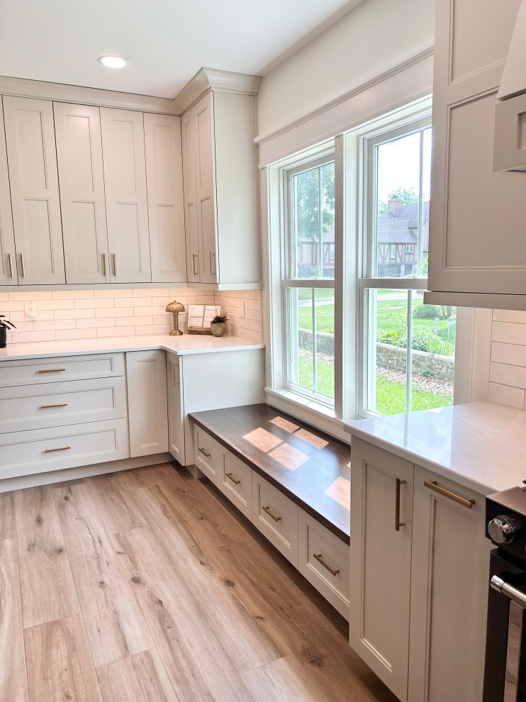 Example of a large transitional u-shaped light wood floor open concept kitchen design with an undermount sink, flat-panel cabinets, white cabinets, quartz countertops, white backsplash, ceramic backsplash, black appliances, an island and white countertops