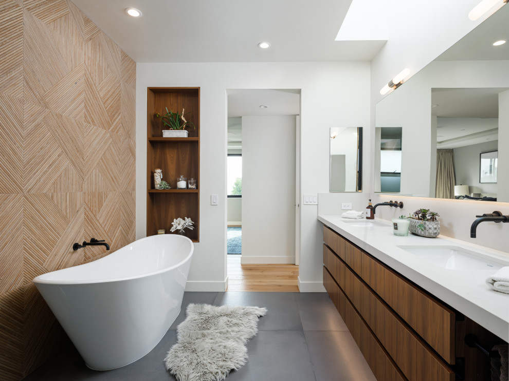 This is an example of a contemporary bathroom in San Diego with flat-panel cabinets, medium wood cabinets, a freestanding tub, beige tile, white walls, an undermount sink, grey floor, white benchtops, a double vanity and a floating vanity.