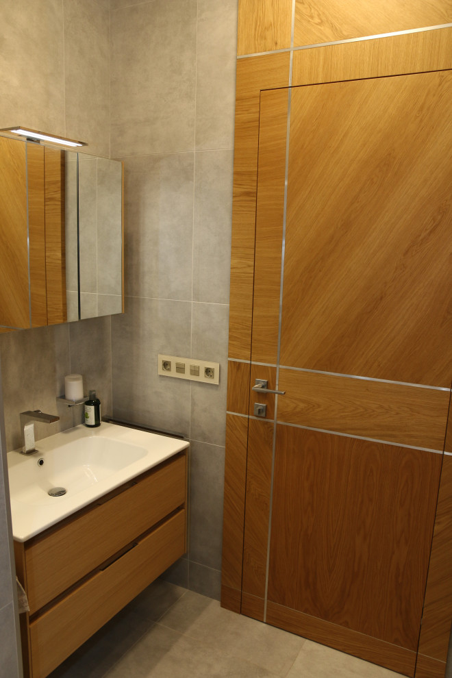 Свежая идея для дизайна: серо-белая ванная комната среднего размера: освещение в современном стиле с плоскими фасадами, фасадами цвета дерева среднего тона, душем в нише, инсталляцией, серой плиткой, керамогранитной плиткой, серыми стенами, полом из керамогранита, душевой кабиной, накладной раковиной, серым полом, душем с распашными дверями, тумбой под одну раковину, подвесной тумбой и многоуровневым потолком - отличное фото интерьера