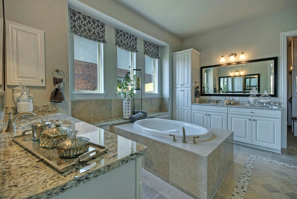 Photo of a mid-sized traditional master bathroom in Austin with a drop-in sink, raised-panel cabinets, white cabinets, granite benchtops, a drop-in tub, an open shower, a one-piece toilet, white tile, porcelain tile, grey walls and porcelain floors.