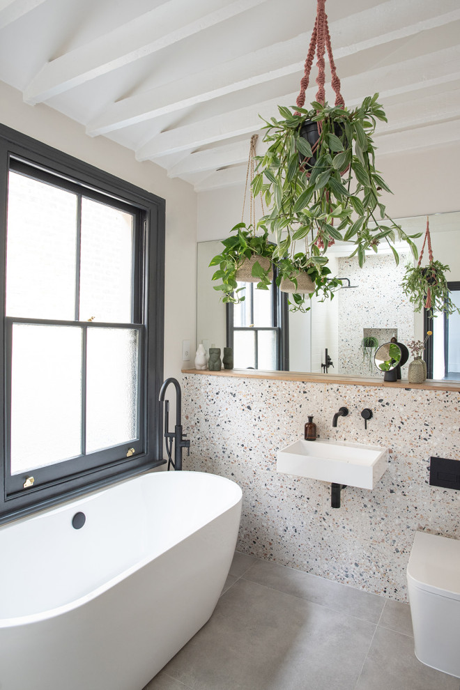 Inspiration for a medium sized contemporary bathroom in London with a freestanding bath, a walk-in shower, a wall mounted toilet, beige tiles, porcelain tiles, multi-coloured walls, cement flooring, a wall-mounted sink, wooden worktops, grey floors, an open shower, a single sink and exposed beams.