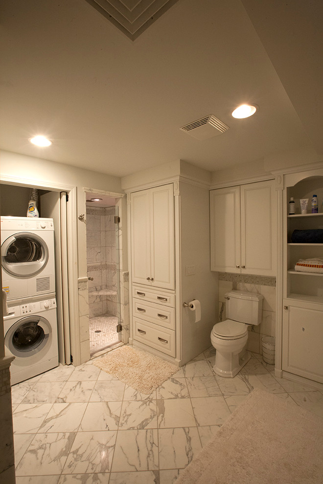 Large transitional l-shaped utility room in New York with white cabinets, marble benchtops, a stacked washer and dryer, raised-panel cabinets, white walls, marble floors and grey floor.