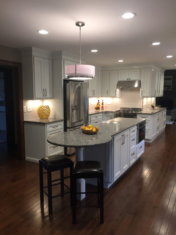 Inspiration for a transitional galley dark wood floor kitchen remodel with an undermount sink, flat-panel cabinets, white cabinets, granite countertops, white backsplash, porcelain backsplash, stainless steel appliances and an island