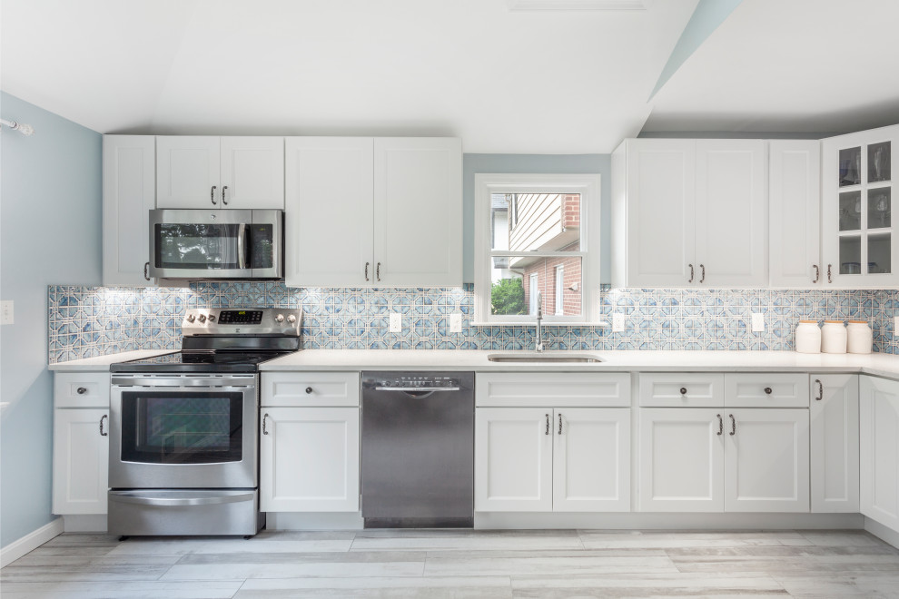 This is an example of a mid-sized mediterranean l-shaped separate kitchen in DC Metro with an undermount sink, recessed-panel cabinets, white cabinets, quartz benchtops, blue splashback, mosaic tile splashback, stainless steel appliances, porcelain floors, no island, grey floor and white benchtop.