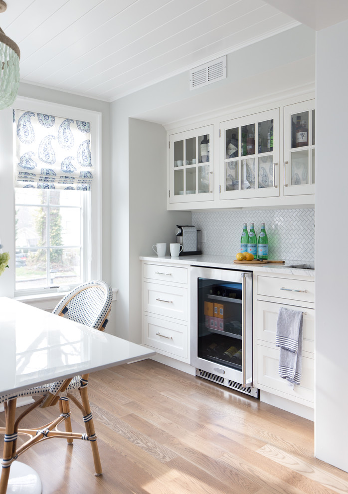 Coastal single-wall light wood floor and beige floor wet bar photo in New York with an undermount sink, glass-front cabinets, white cabinets and white backsplash