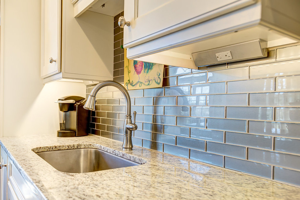 Example of a mid-sized transitional l-shaped light wood floor open concept kitchen design in Birmingham with a single-bowl sink, flat-panel cabinets, white cabinets, granite countertops, green backsplash, glass tile backsplash, stainless steel appliances and an island