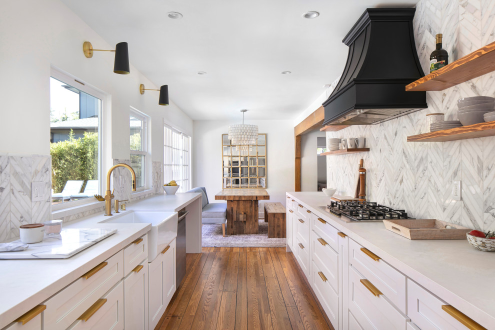 This is an example of a medium sized traditional galley kitchen/diner in Los Angeles with a belfast sink, shaker cabinets, white cabinets, engineered stone countertops, multi-coloured splashback, marble splashback, stainless steel appliances, medium hardwood flooring, no island, brown floors and grey worktops.