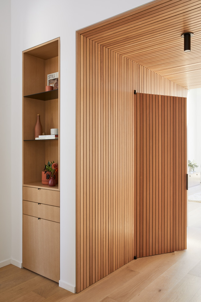 Foto de distribuidor abovedado moderno de tamaño medio con paredes blancas, suelo de madera clara, puerta pivotante, puerta de madera clara, suelo marrón y madera