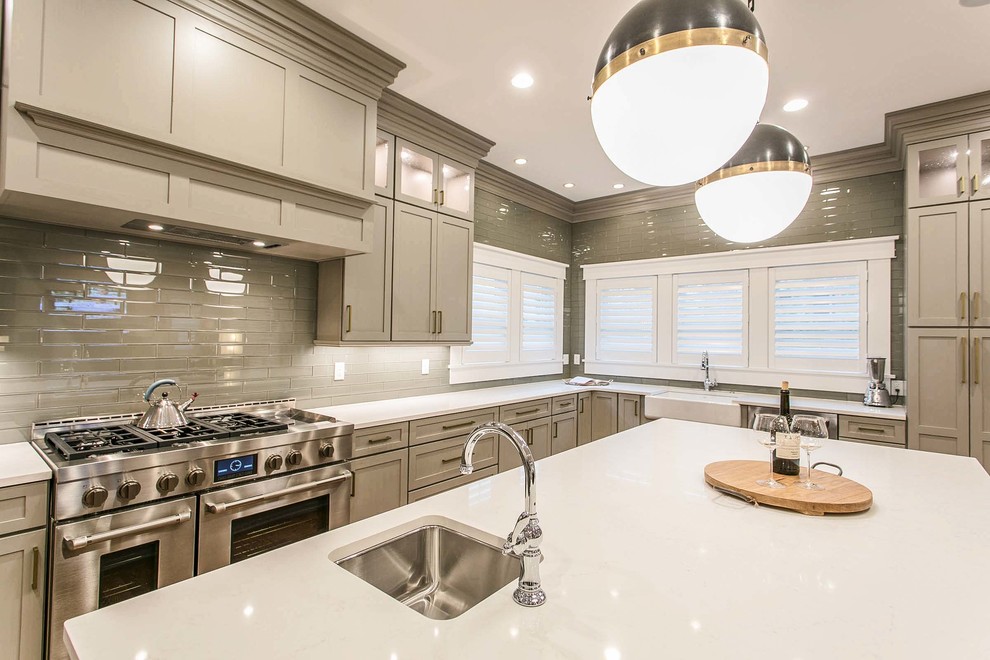 Large transitional l-shaped open concept kitchen photo with a farmhouse sink, shaker cabinets, gray cabinets, quartz countertops, gray backsplash, glass tile backsplash, stainless steel appliances, an island and white countertops