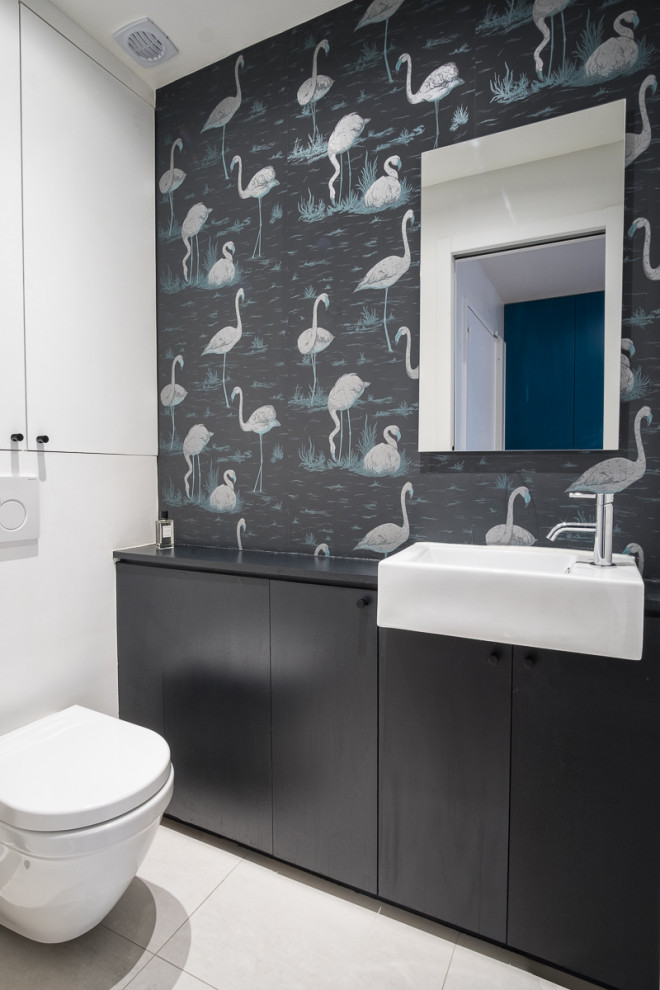 This is an example of a mid-sized contemporary 3/4 bathroom in Paris with flat-panel cabinets, black cabinets, a wall-mount toilet, multi-coloured walls, porcelain floors, a drop-in sink, grey floor, black benchtops, a single vanity, a built-in vanity and wallpaper.
