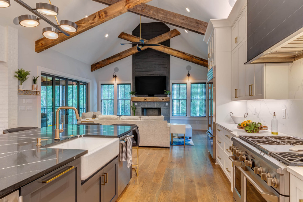 Inspiration for a large modern l-shaped open plan kitchen in Atlanta with a farmhouse sink, shaker cabinets, white cabinets, quartz benchtops, white splashback, engineered quartz splashback, stainless steel appliances, medium hardwood floors, with island, brown floor, black benchtop and exposed beam.