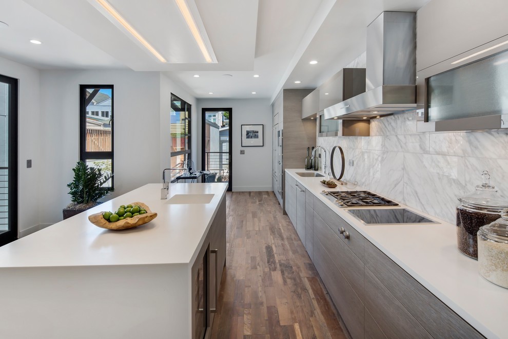 Contemporary galley kitchen in San Francisco with an integrated sink, flat-panel cabinets, grey cabinets, white splashback, medium hardwood floors, with island, brown floor and white benchtop.