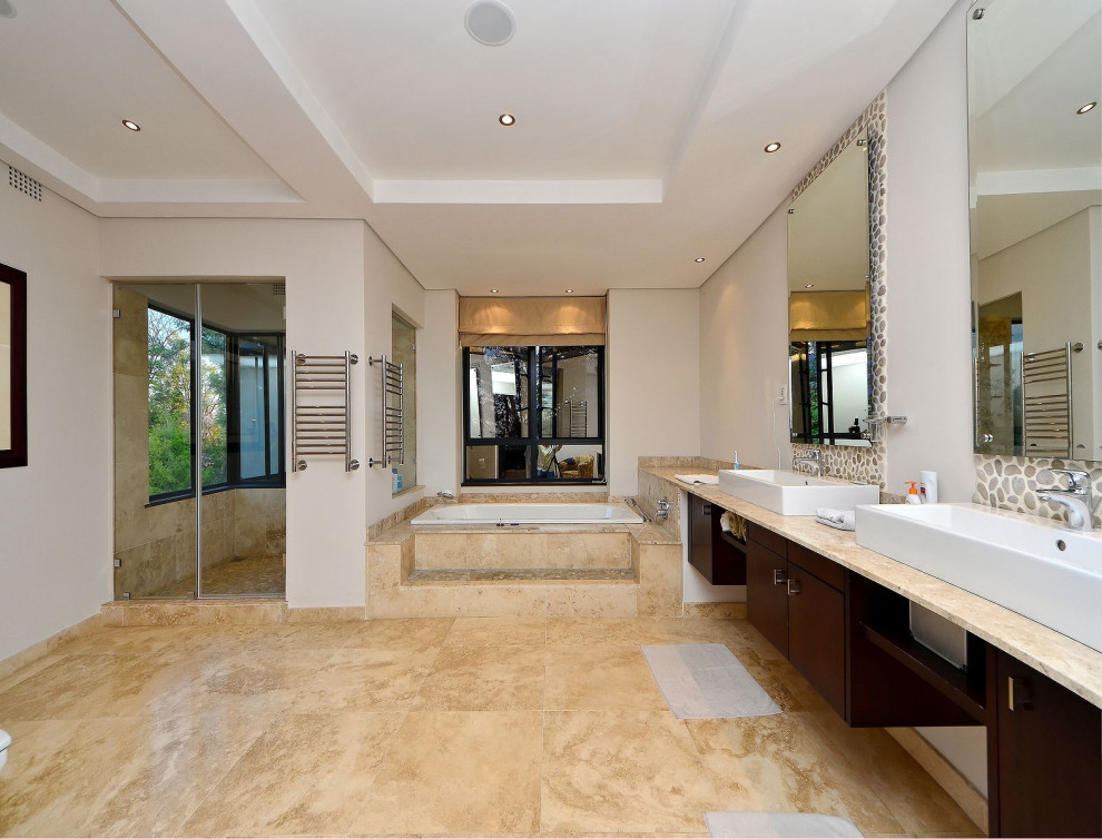 Design ideas for a large contemporary master bathroom in Other with flat-panel cabinets, dark wood cabinets, a drop-in tub, an open shower, beige tile, travertine, white walls, travertine floors, marble benchtops, beige floor, a hinged shower door, beige benchtops, a double vanity and a built-in vanity.