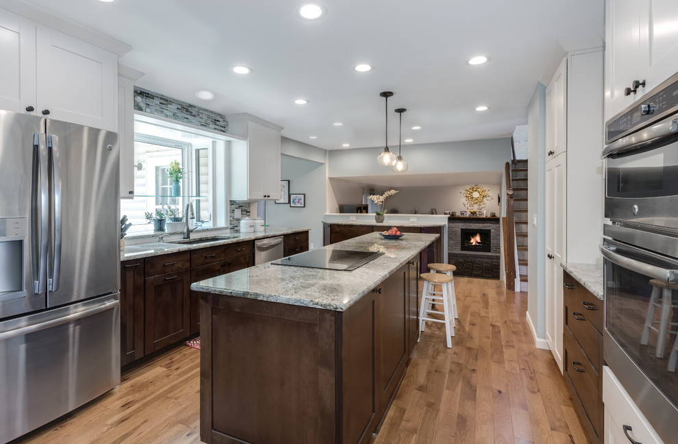 This is an example of a mid-sized transitional galley eat-in kitchen in Denver with an undermount sink, shaker cabinets, white cabinets, granite benchtops, blue splashback, glass tile splashback, stainless steel appliances, medium hardwood floors, with island, brown floor and beige benchtop.