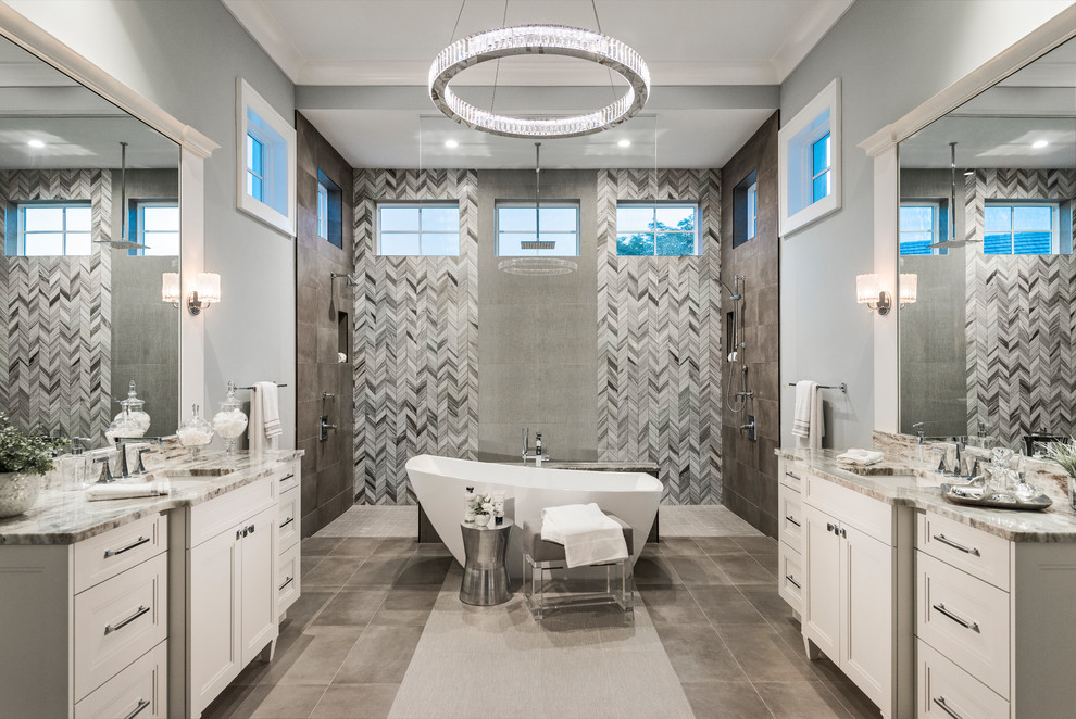This is an example of a transitional master bathroom in Miami with recessed-panel cabinets, white cabinets, a freestanding tub, a double shower, gray tile, grey walls, an undermount sink, grey floor, an open shower and beige benchtops.