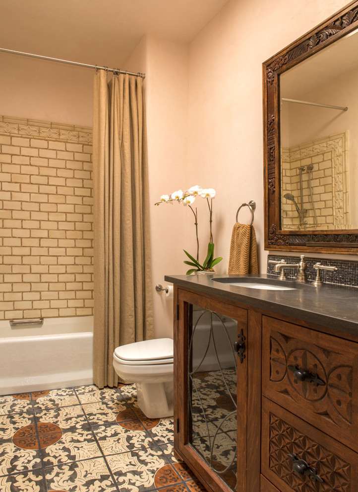 This is an example of a mid-sized traditional master bathroom in Albuquerque with an undermount sink, furniture-like cabinets, medium wood cabinets, an alcove tub, a shower/bathtub combo, a one-piece toilet, multi-coloured tile, terra-cotta tile, beige walls and terra-cotta floors.