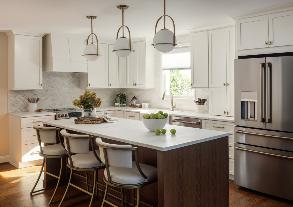 Photo of a classic l-shaped kitchen in DC Metro with a belfast sink, shaker cabinets, white cabinets, white splashback, stainless steel appliances, medium hardwood flooring, an island, brown floors and white worktops.