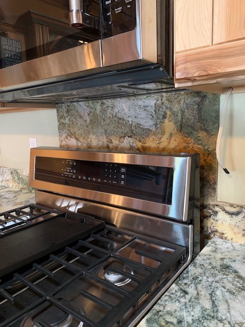 Inspiration for a mid-sized rustic medium tone wood floor and brown floor open concept kitchen remodel with an undermount sink, flat-panel cabinets, light wood cabinets, granite countertops, gray backsplash, stone slab backsplash, stainless steel appliances and gray countertops