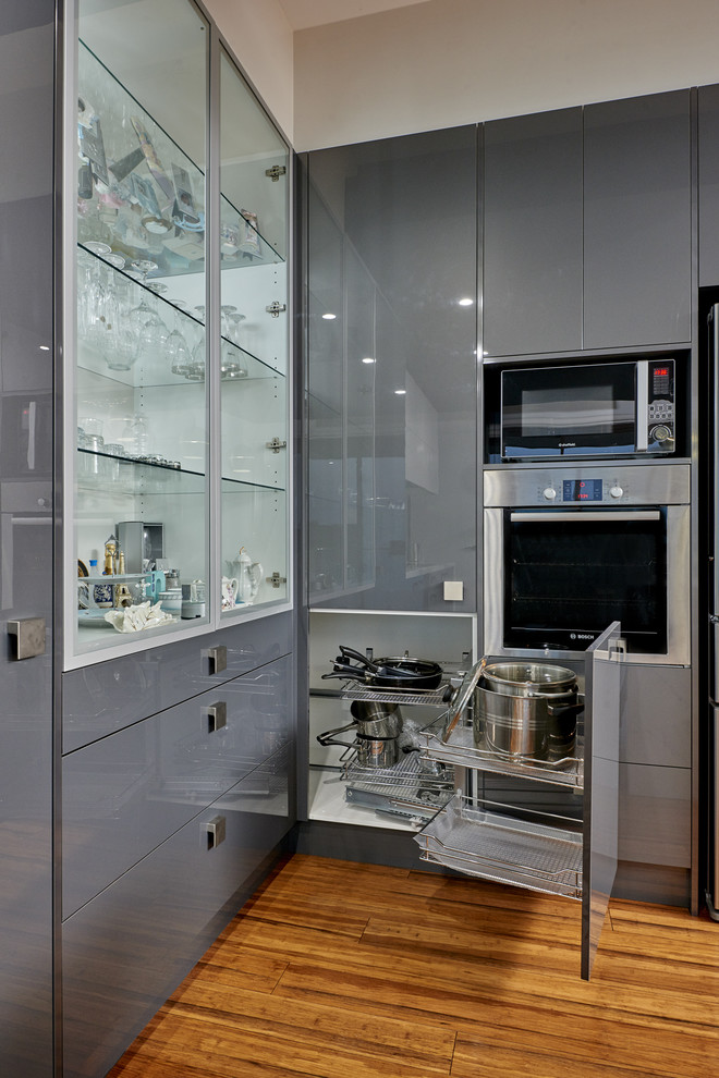 This is an example of a large contemporary l-shaped eat-in kitchen in Melbourne with a double-bowl sink, flat-panel cabinets, marble benchtops, green splashback, glass sheet splashback, stainless steel appliances, medium hardwood floors and with island.