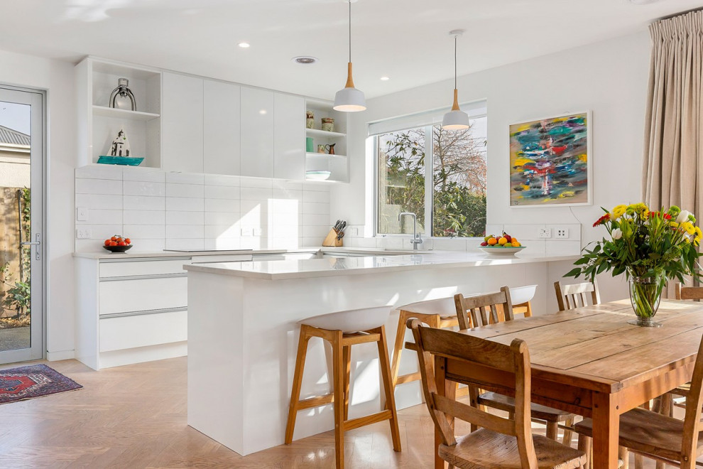 Mid-sized contemporary galley eat-in kitchen in Christchurch with an undermount sink, flat-panel cabinets, white cabinets, white splashback, a peninsula, brown floor and white benchtop.