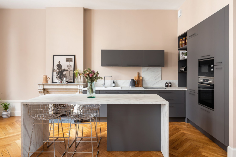 Design ideas for a medium sized contemporary open plan kitchen in Saint-Etienne with a built-in sink, flat-panel cabinets, grey cabinets, laminate countertops, white splashback, black appliances, an island and white worktops.