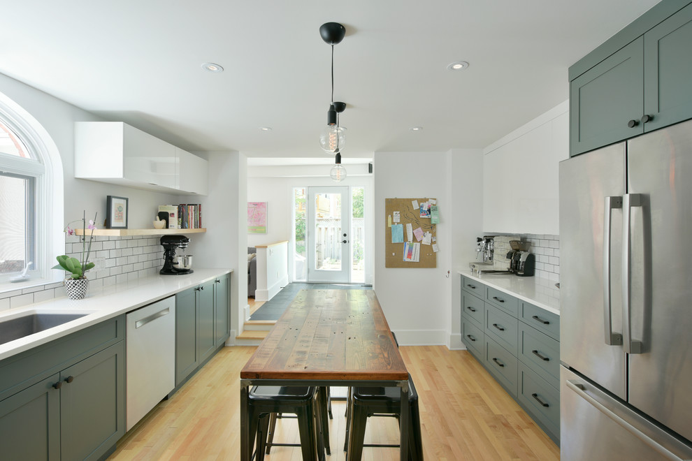 Inspiration for a large transitional galley separate kitchen in Ottawa with shaker cabinets, green cabinets, with island, an undermount sink, solid surface benchtops, white splashback, subway tile splashback, stainless steel appliances and light hardwood floors.