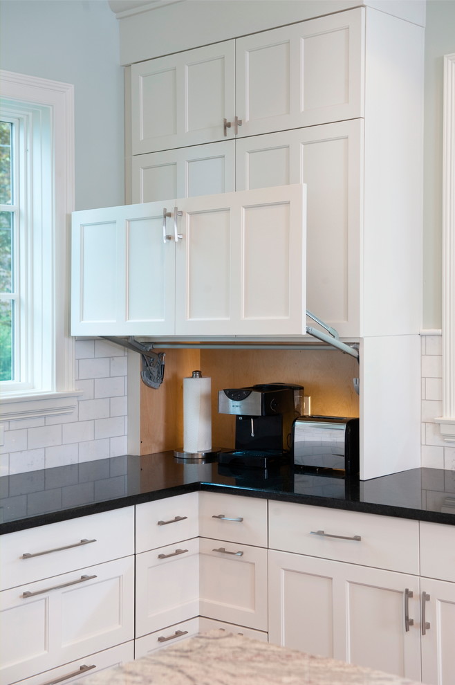 This is an example of a large traditional u-shaped kitchen in Chicago with an undermount sink, recessed-panel cabinets, white cabinets, granite benchtops, white splashback, subway tile splashback, white appliances, dark hardwood floors and with island.