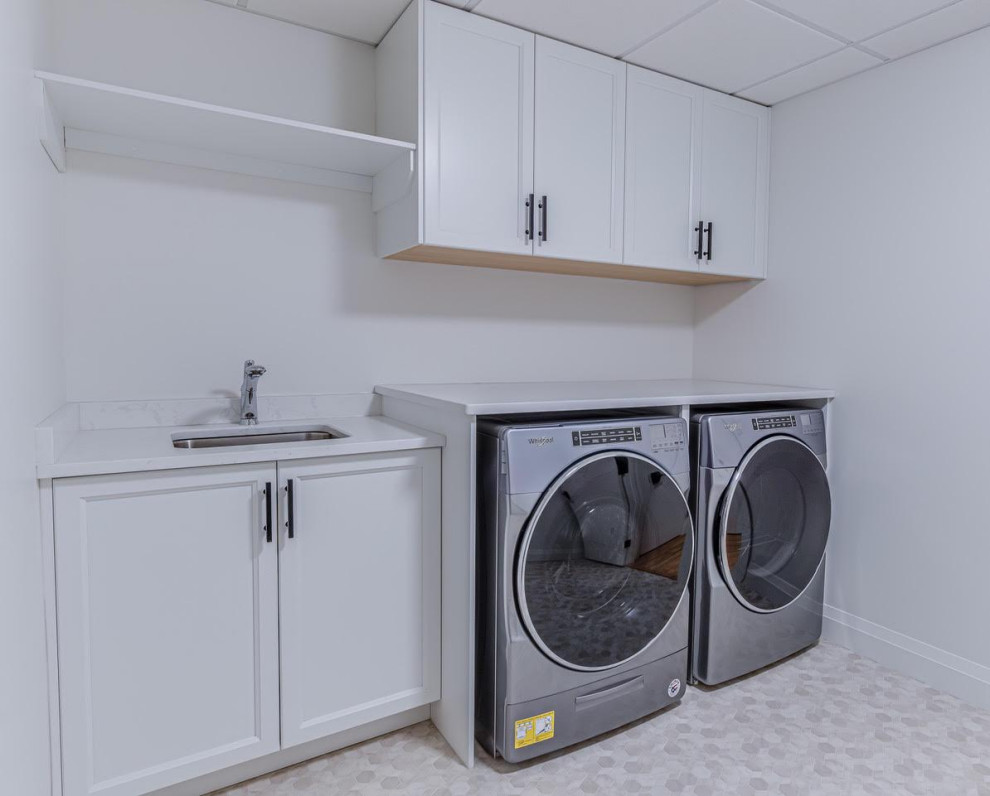 Idéer för små lantliga vitt tvättstugor enbart för tvätt, med en undermonterad diskho, luckor med infälld panel, vita skåp, granitbänkskiva, vita väggar, en tvättmaskin och torktumlare bredvid varandra, grått golv och laminatgolv