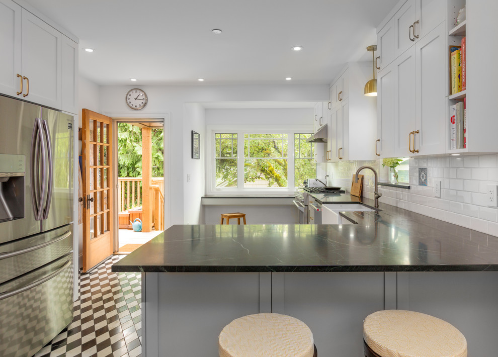 Inspiration for a mid-sized arts and crafts l-shaped eat-in kitchen in Vancouver with a farmhouse sink, shaker cabinets, grey cabinets, soapstone benchtops, white splashback, subway tile splashback, stainless steel appliances, marble floors, a peninsula, black floor and black benchtop.