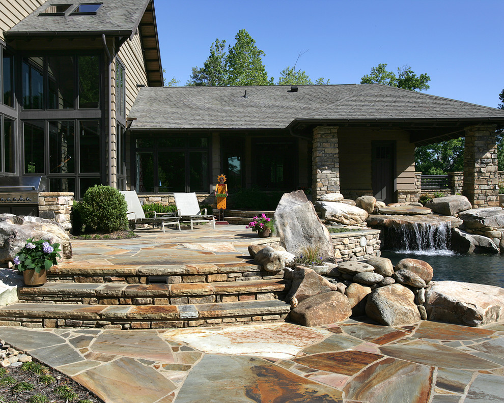 Photo of a large traditional backyard custom-shaped pool in Other with a water feature and natural stone pavers.